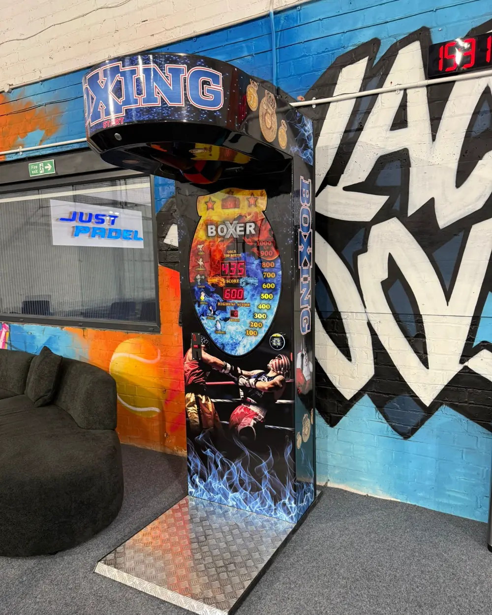 A Haymaker Arcade boxing machine installed at Just Padel, lit up with its score display showing and a ramp up to the plate